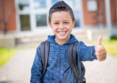 Young child having thumbs up in front of school